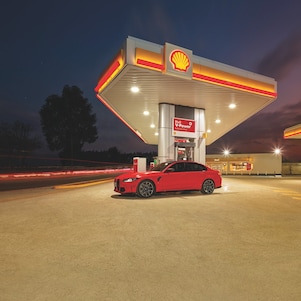 A red BWM M3 parked on a Shell Forecourt during dusk
