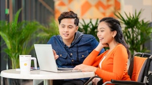 Two people are sitting at a round table with a laptop in front of them