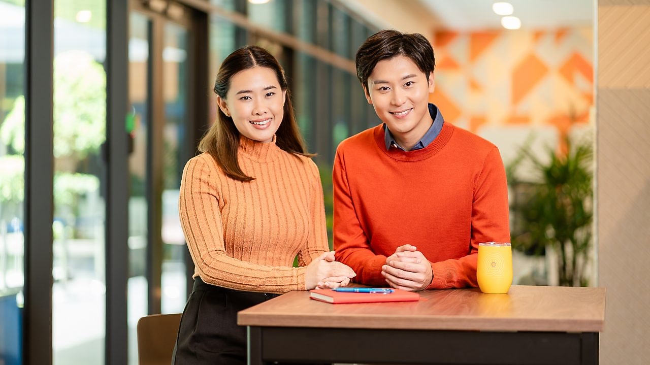 Two individuals are standing side by side at a high table in a modern indoor setting
