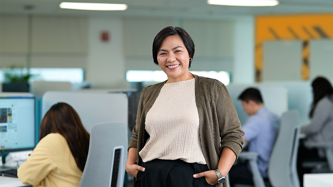 person stands confidently in a modern office environment with hands in pockets