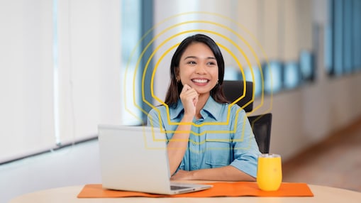 An female employee sitting at a table with her hand on her chin and smiling. She has a laptop in front of her