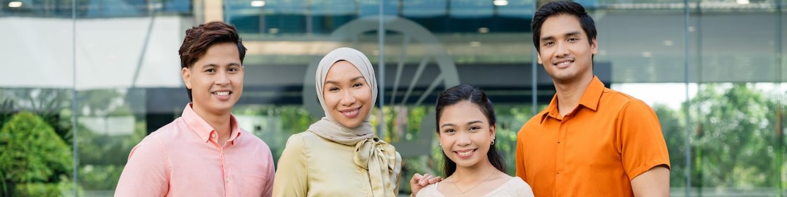 Four people standing together outdoors in front of a modern glass building, wearing casual and semi-formal outfits.