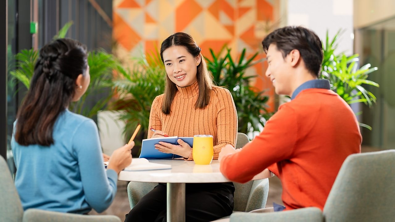 Three employees seated at a table and having a work-related discussion