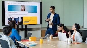 Person presenting a data science careers webpage on a large screen to a group seated at a conference table with laptops.