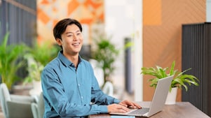 A male employee smiling while looking elsewhere, and a laptop is in front of him