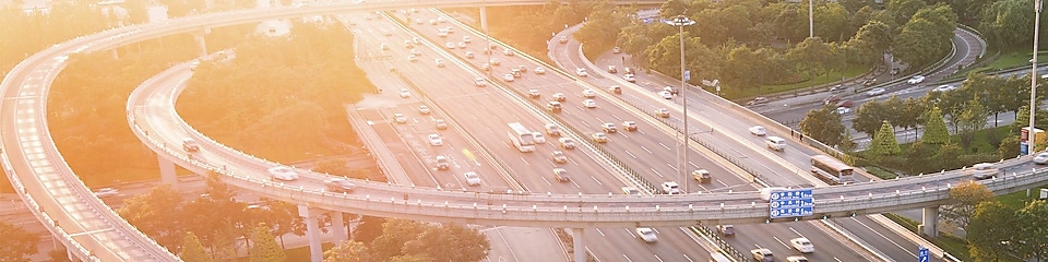 Image of vehicles on motorway/highway with sunset and trees in the background.