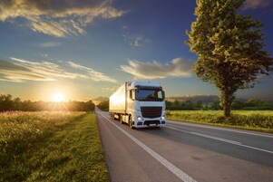 Trucks driving down a highway in green scenery and a blue sky.
