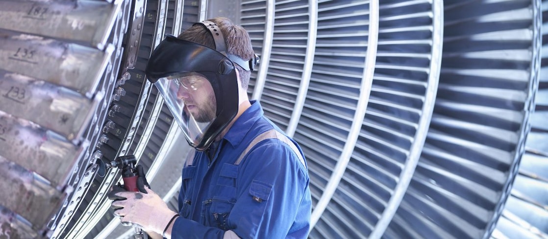 Engineer repairing steam turbine blade with grinder in workshop