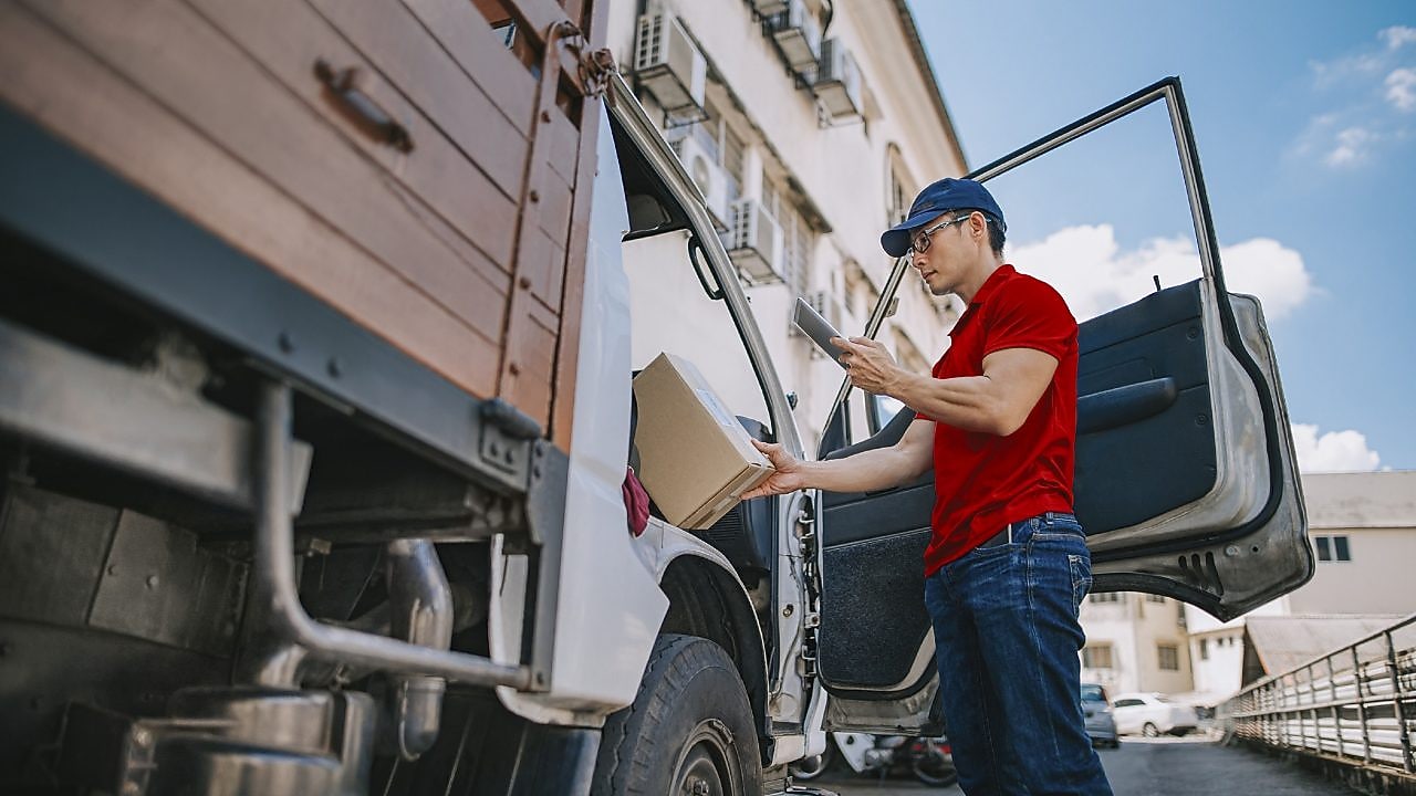 Delivery man standing at the door of truck checking his deliveries on phone