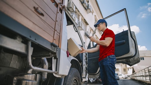 Delivery man standing at the door of truck checking his deliveries on phone