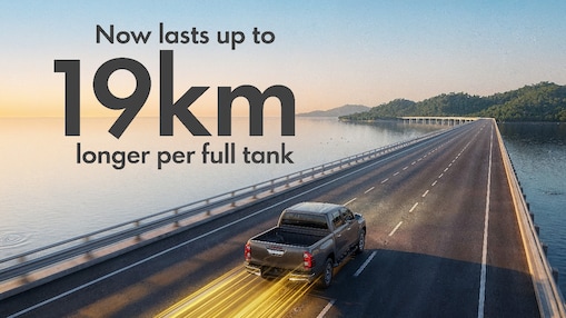 Grey Pick-Up Truck driving on a bridge with the sea around it and text saying “Now lasts up to 19km longer per full tank” on the left side of the image
