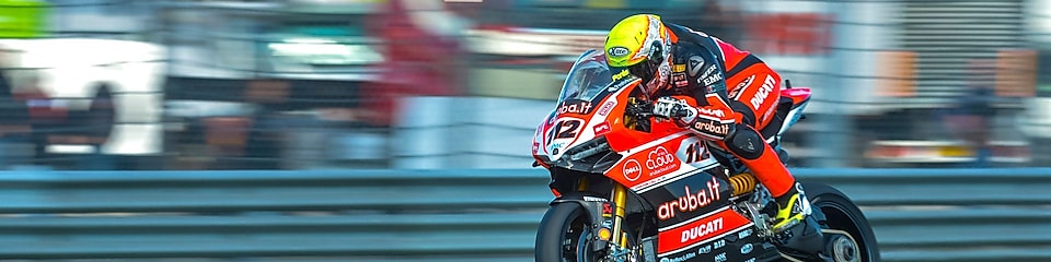Ducati superbike with rider racing on a track with lorries in the background